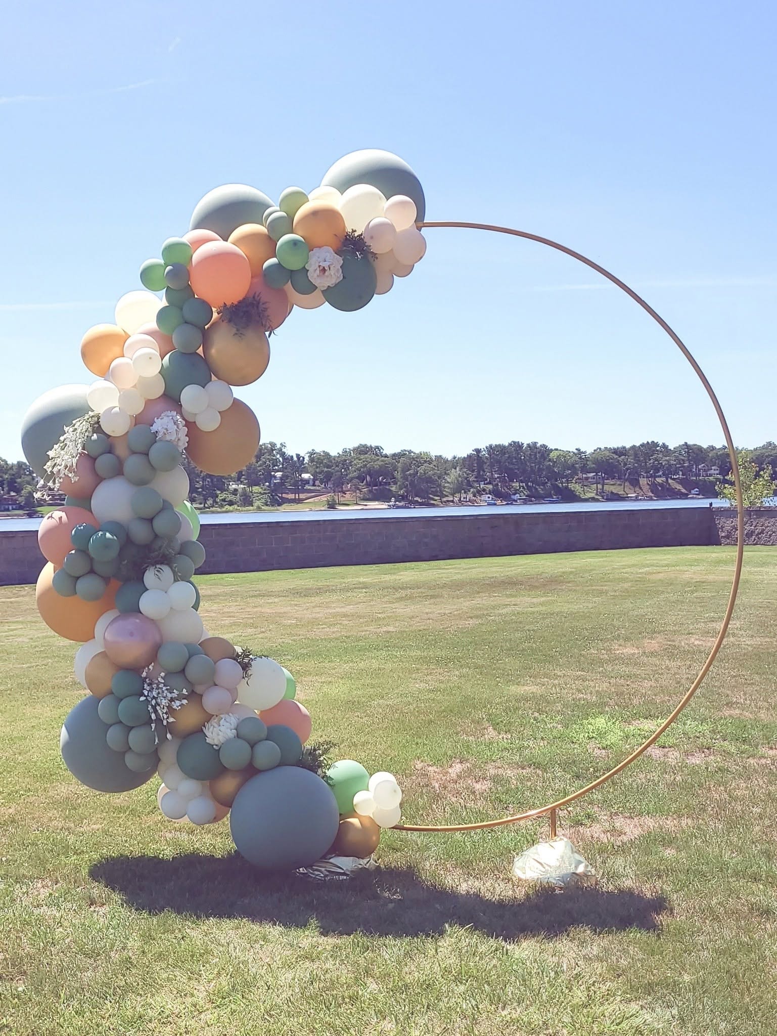 Pastel sage coral and cream balloon hoop arch outdoors by the water