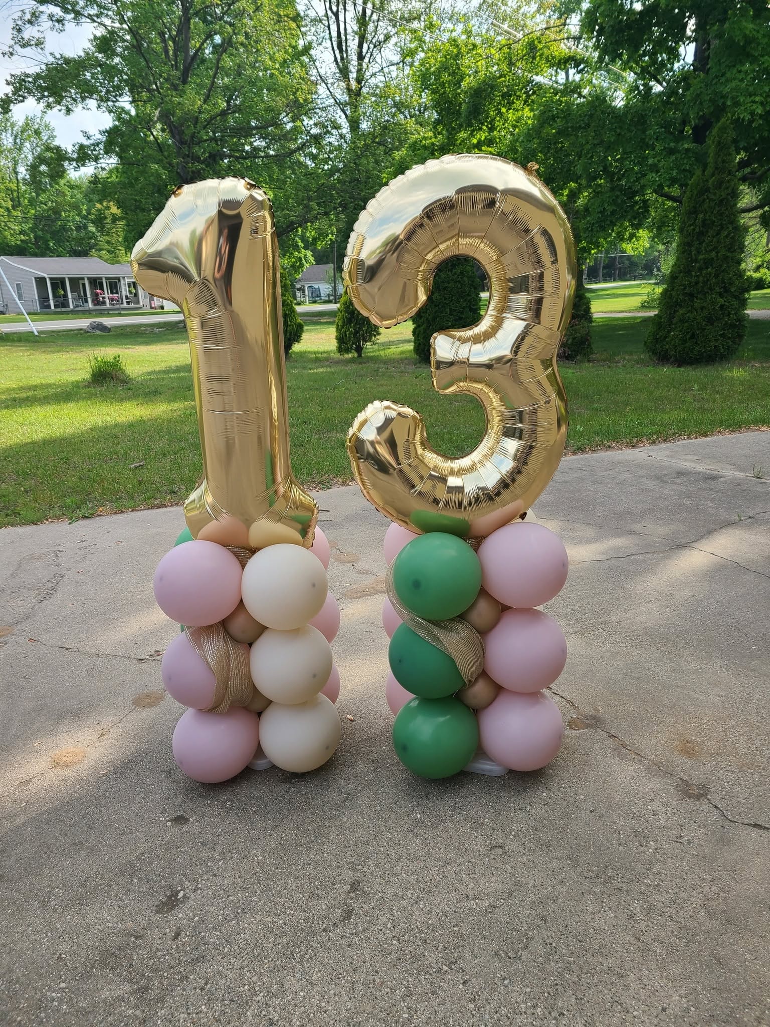Gold number 13 foil balloons on pink white and green balloon columns
