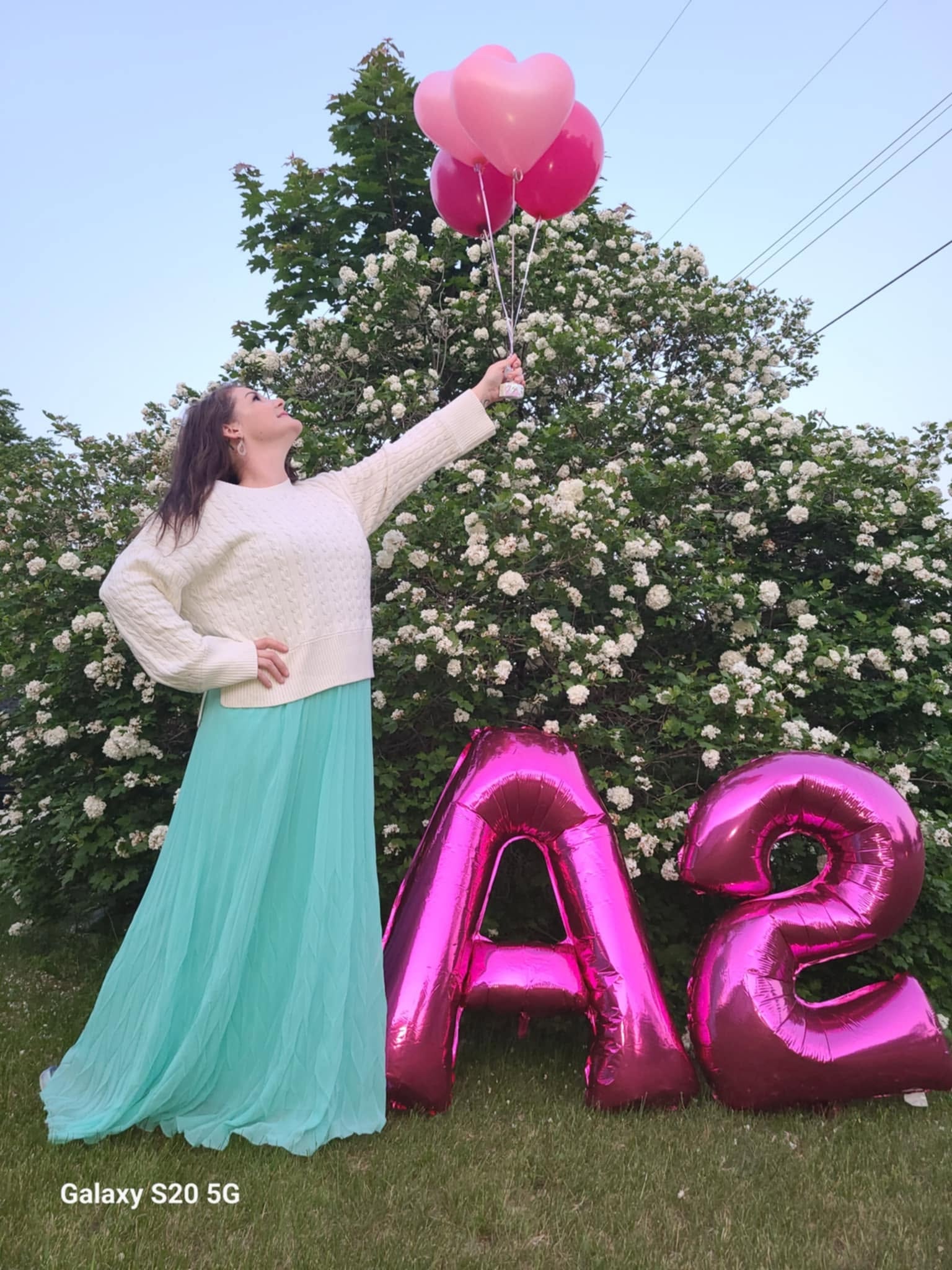 Woman holding pink heart balloons next to A2 letter balloons outdoors