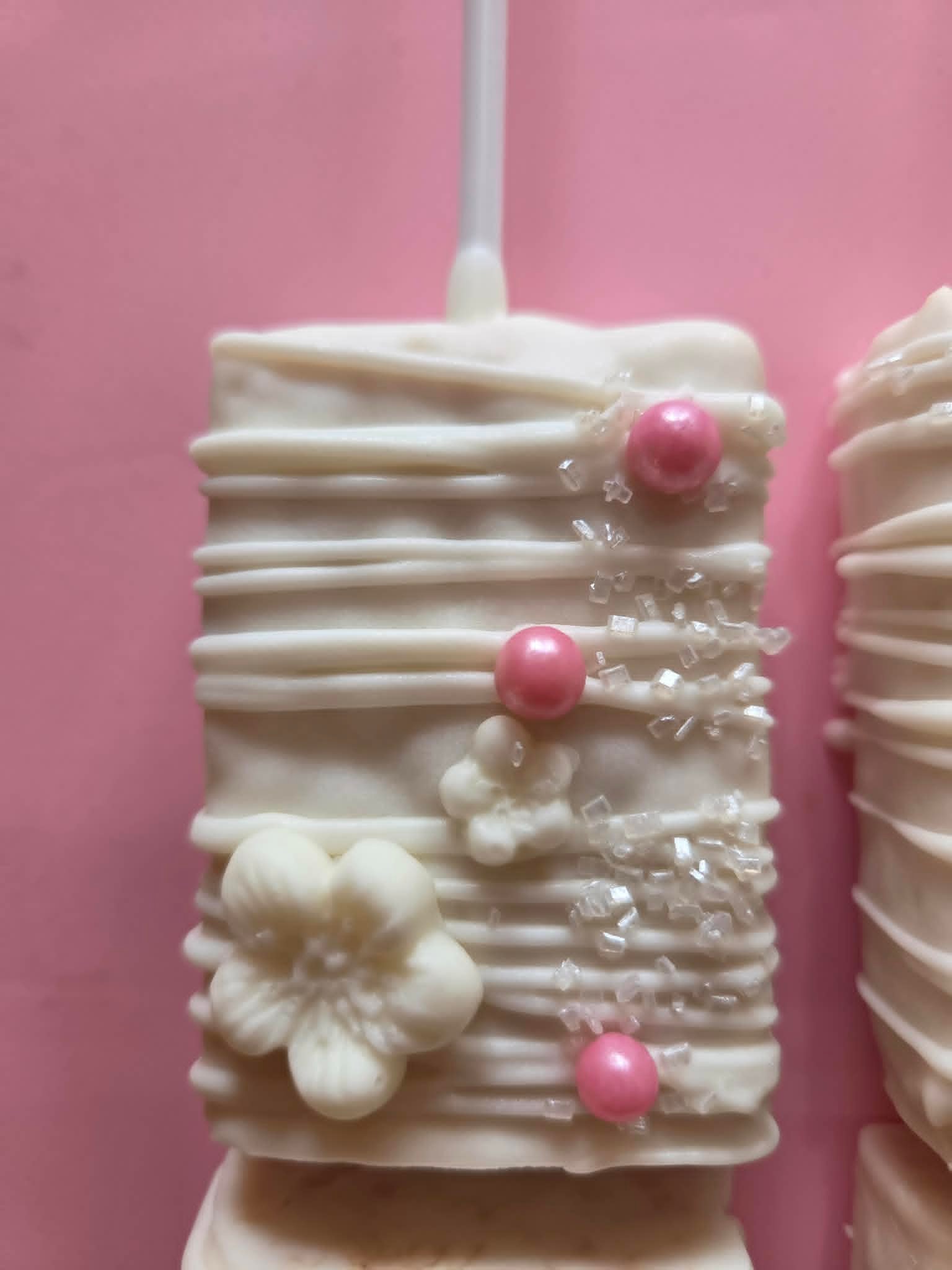 White chocolate Oreo pop with white flower, pink pearls and crystal sugar close-up
