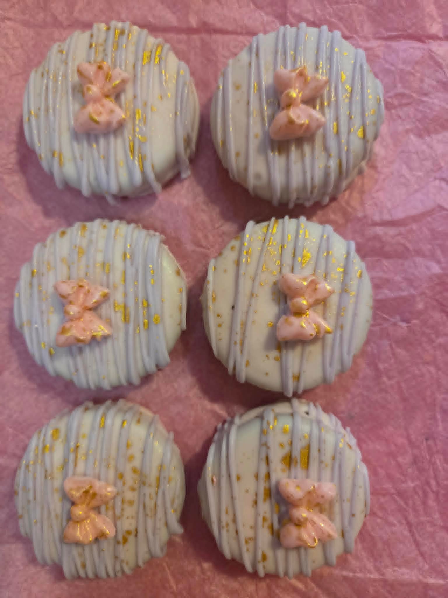 White chocolate Oreo pops with gold flake and pink bow toppers arranged in a grid