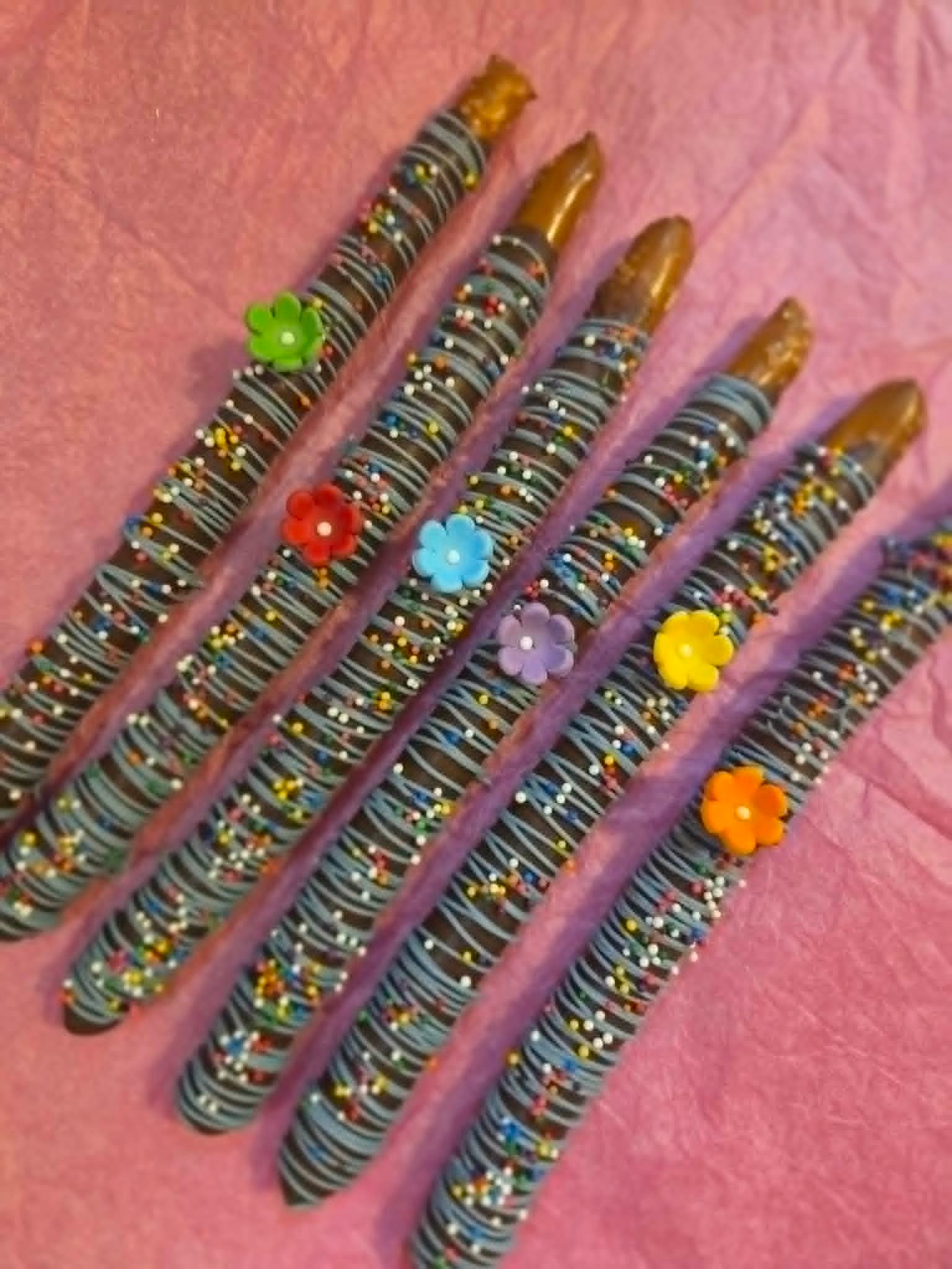 Chocolate-dipped pretzel rods with blue drizzle and colorful flower toppers