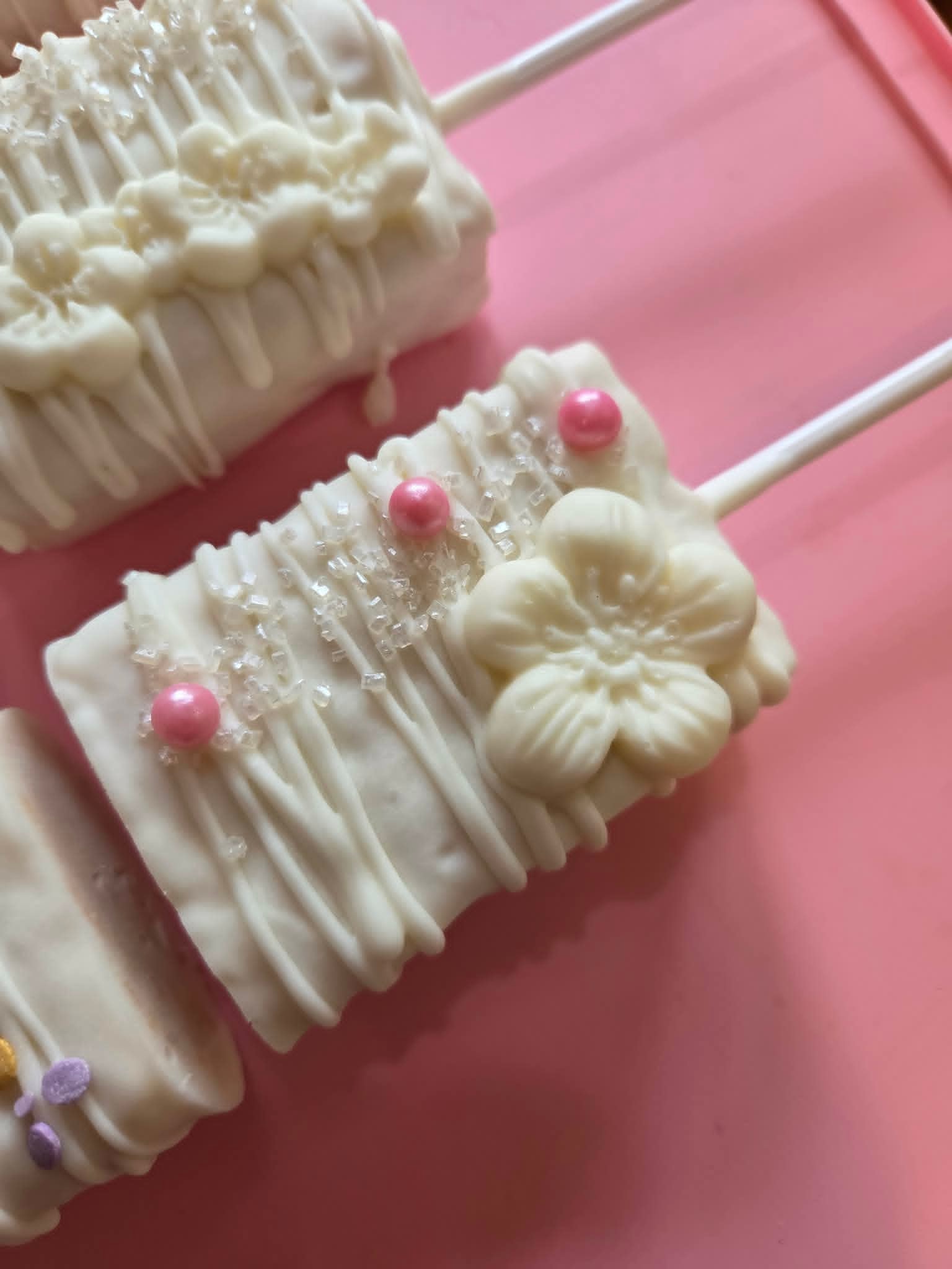 Close-up of white chocolate rice krispy pop with pink pearl and flower topper on pink background