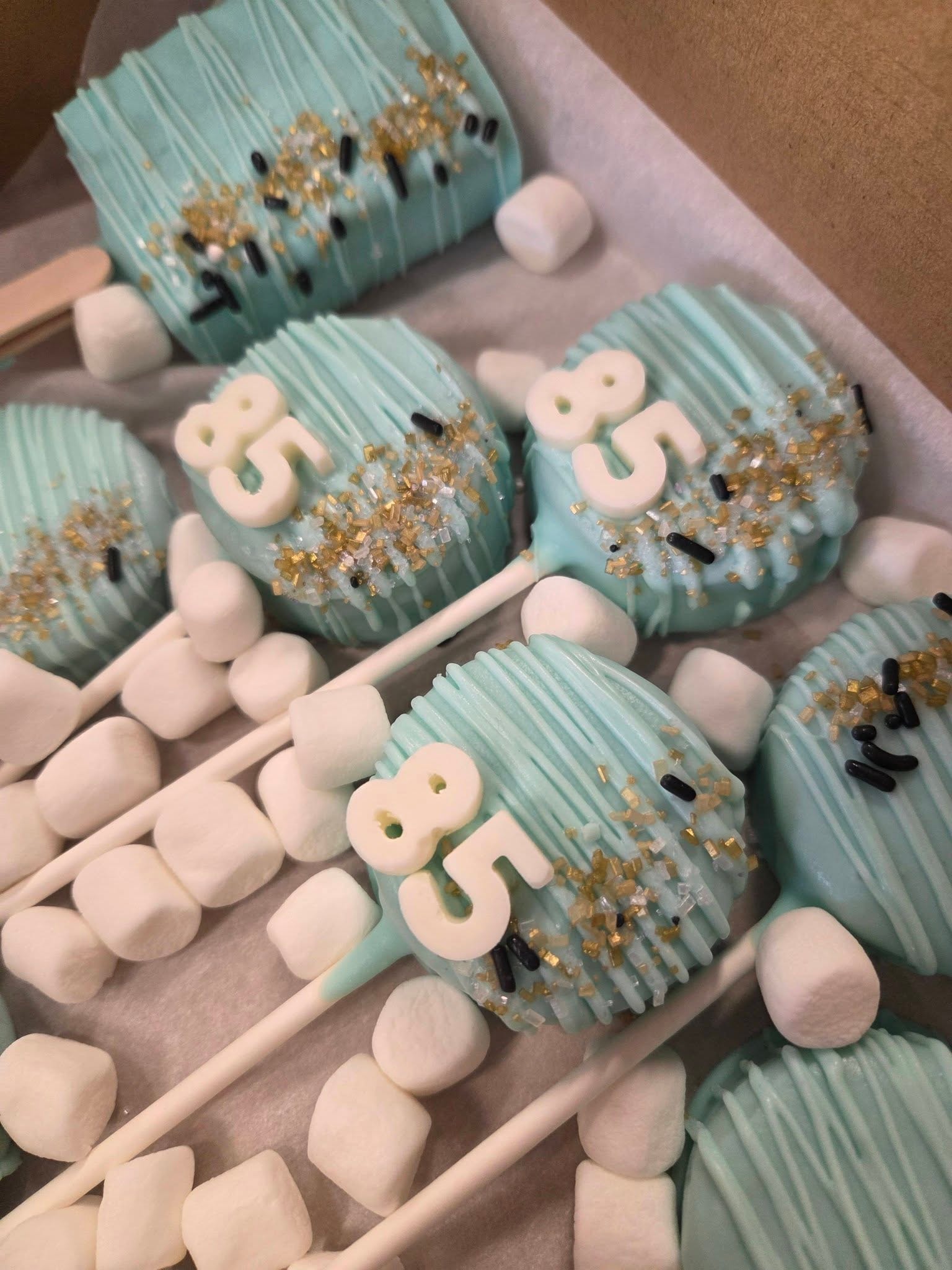 Teal Oreo pops with number 85 fondant toppers and gold sprinkles