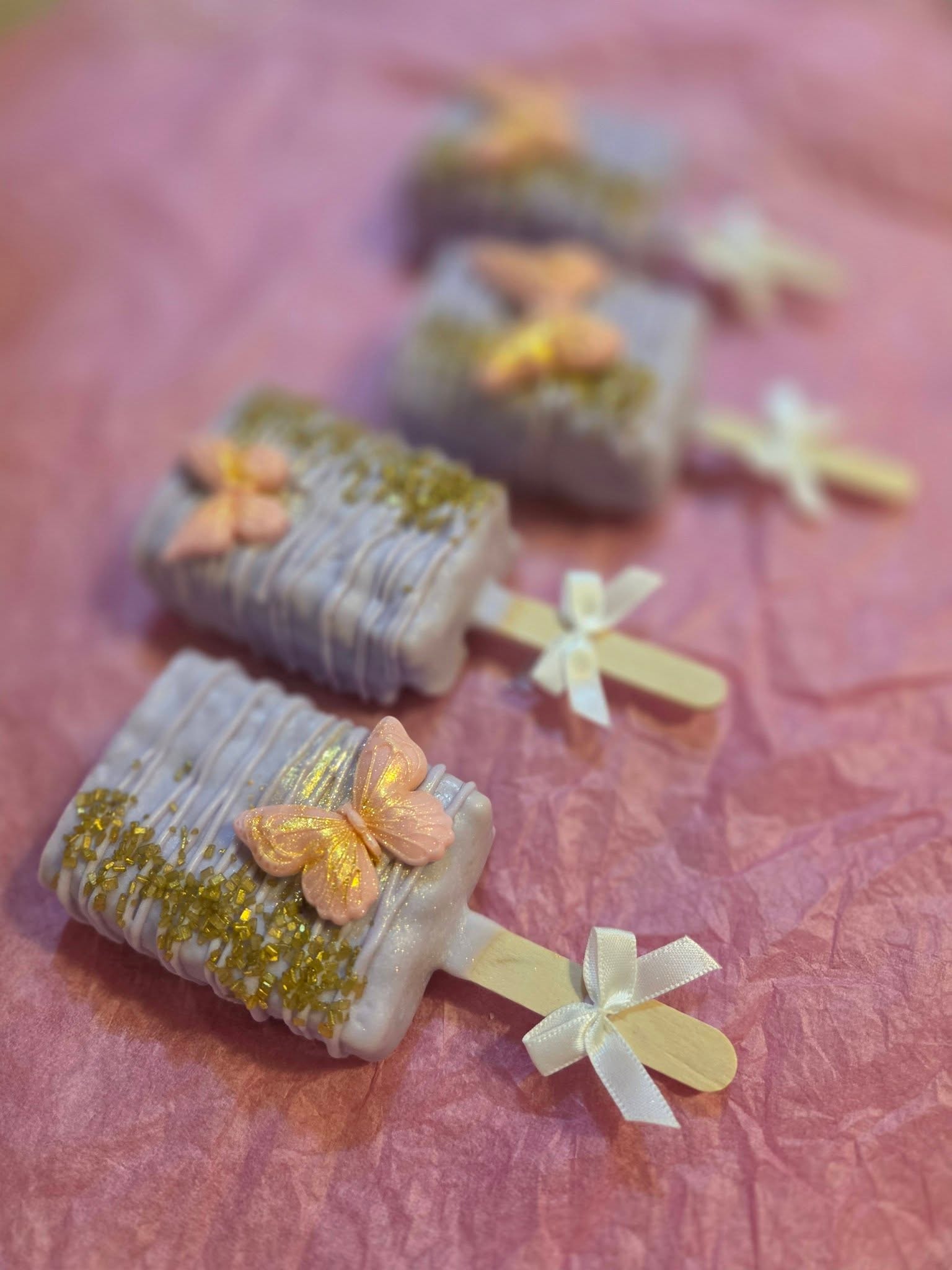 Lavender cakesicles with butterfly toppers and gold glitter, tied with ribbon bows